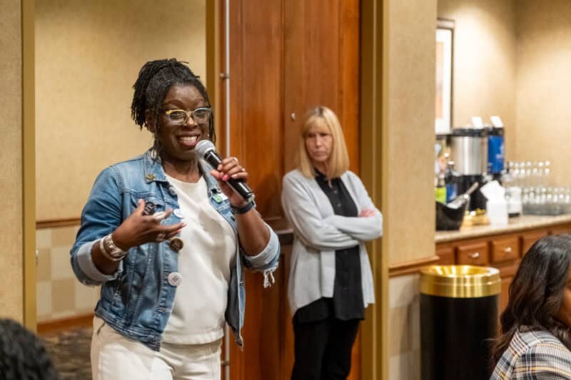 CHCM CEO Riisa Rawlins holding microphone and talking with her hands for emphasis